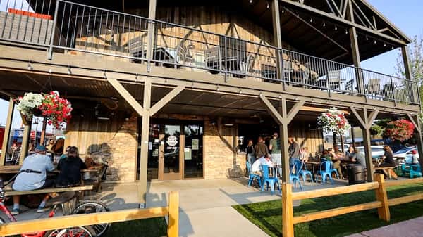 Exterior view of Otto's Landing restaurant with rustic wood siding, hanging flower baskets, and groups dining on the front patio under covered seating.