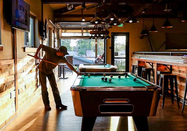 Guest playing a game of pool in Otto's Landing's rustic game room with wood accents, flat-screen TVs, and relaxed bar seating.