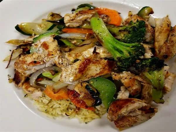 mixed veggie stir fry with broccoli, zucchini, peppers, onions and zucchini served over rice with chicken on top