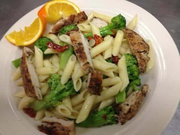 chicken over penne pasta with broccoli and a slice of orange on a white dish