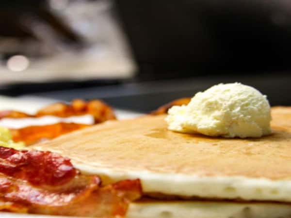1a double stack of pancakes topped with butter and bacon on the side