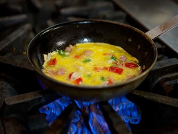 omelette with ham and peppers being cooked in a skillet