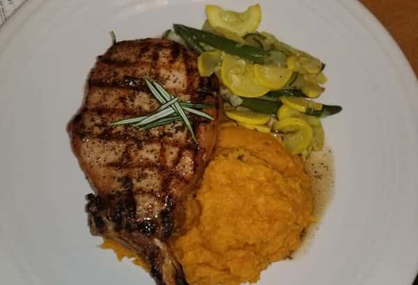 a lamb chop with a side of string beans, zucchini and yams