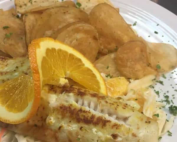 a grilled fish with a side of potato chips and an orange wedge