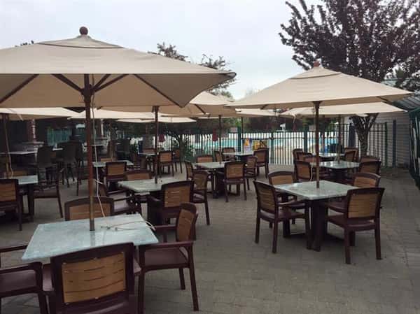outdoor seating area with 11 tables and four chairs at each table with a beige umbrella at each table