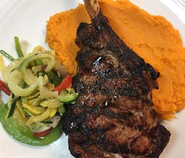 a lamb chop with a side of mixed vegetables and yams