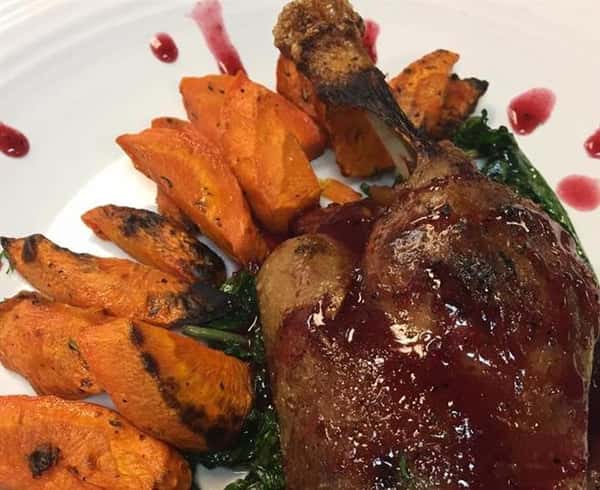a lamb chop with barbecue sausace on top on a bed of cooked spinach and sweet potato fries