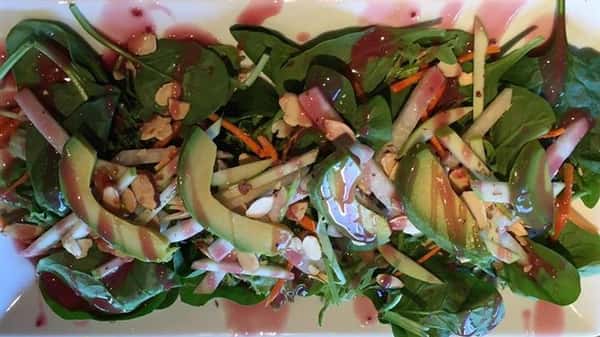 a salad with spinach, avocado, cheese, carrots, almonds, and a pink vinaigrette