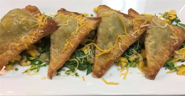 three empanadas on a plate on a bed of lettuce and corn covered in shredded cheese