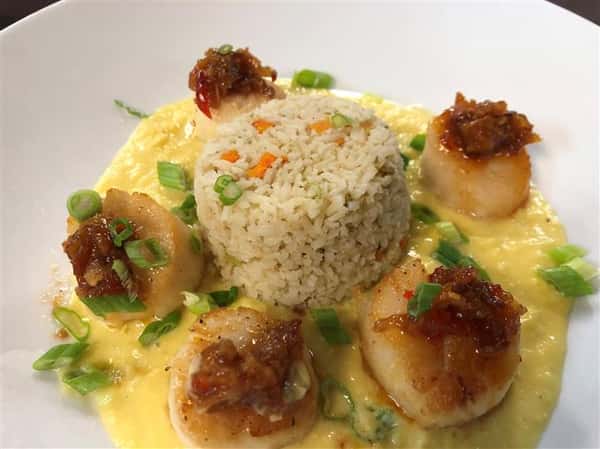 a scoop of rice surrounded by five scallops in a pool of yellow sauce