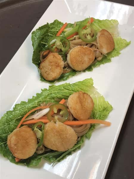 two pieces of lettuce with three scallops on each with shredded carrot and jalapeno slices