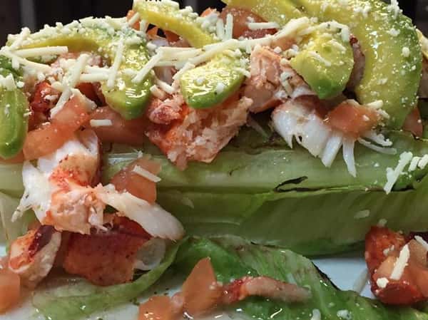 a bed of lettuce with lobster meat, tomato, cheese, and avocado on top