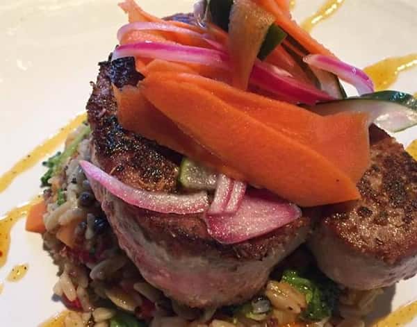 a steak on a bed of mixed vegetables with red onion and carrots on top
