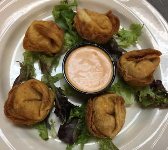five fried wontons on a bed of lettuce with a side of orange dipping sauce