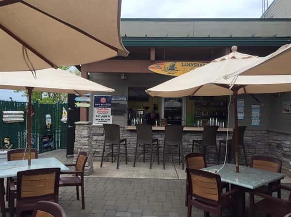 outdoor seating area of two tables with four chairs at each table, two umbrellas and a bar with five stools at it