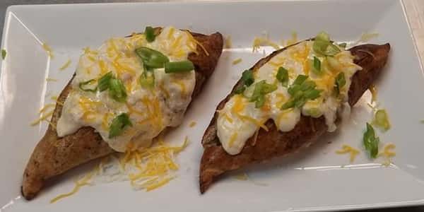 two baked potaoes with white sauce on top with cheese and scallions