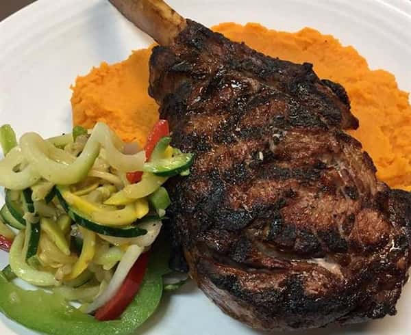 a lamb chop with a side of mixed vegetables and yams