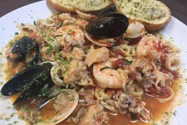 pasta with shrimp, mussels, and clams in an orange sauce with a side of garlic bread