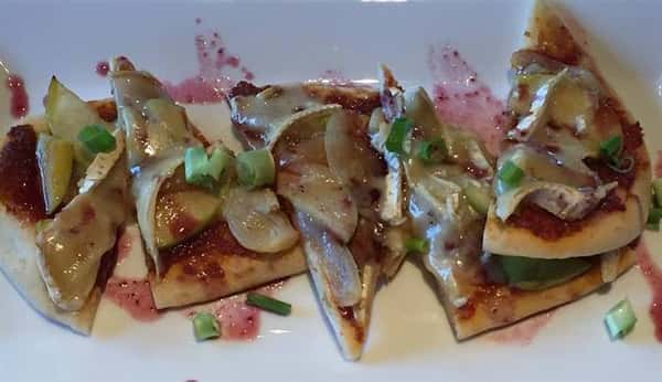 a flatbread cut into five pieces with pink dressing on it and artichokes