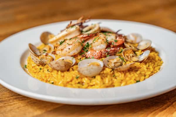 Creamy saffron risotto generously topped with clams, shrimp, and calamari, plated on white china—ideal for coastal Italian cuisine or fine dining menus.