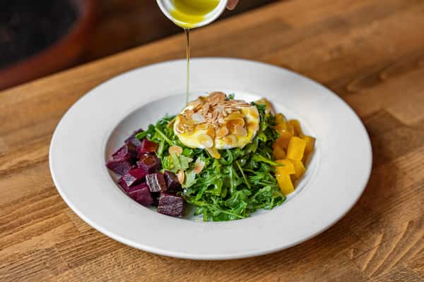 Arugula beet salad topped with goat cheese, slivered almonds, and a drizzle of olive oil, served with roasted golden and red beets.
