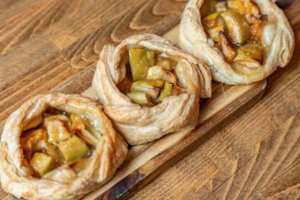 Angled view of rustic apple pastries with golden, flaky layers and gooey apple filling, ideal for showcasing autumn bakery offerings or homemade desserts.