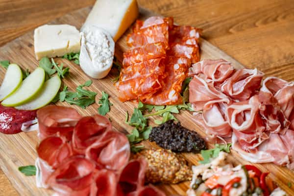 Artisan charcuterie board featuring cured meats like prosciutto and salami, assorted cheeses, fresh pear slices, tapenade, mustard, and arugula—ideal for upscale Italian dining or wine bar menus.