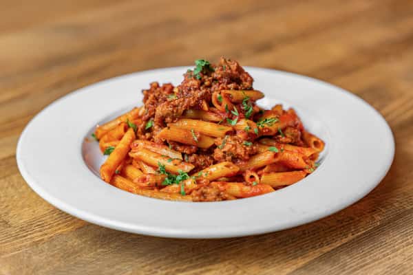 Overhead view of penne pasta in a rich tomato and sausage ragù, topped with chopped parsley—classic Italian comfort food with rustic presentation.