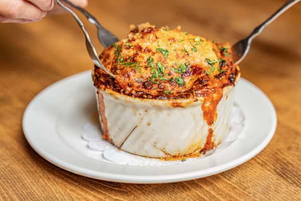Baked lasagna served in a ceramic ramekin, with crispy, golden cheese crust being cut into—ideal for showcasing Italian comfort food or homemade-style dining.