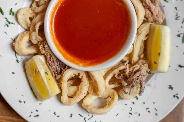 Golden fried calamari rings with lemon wedges and a bowl of marinara dipping sauce, elegantly plated with herb garnish.