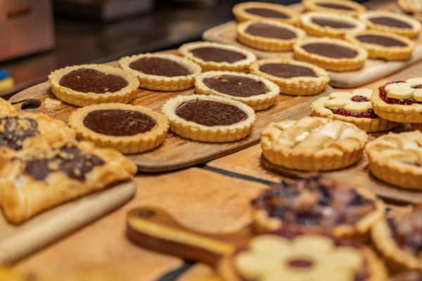 Variety of freshly baked tarts and pastries on wooden boards, featuring rich chocolate-filled tartlets, lattice-topped mini pies, and jam-filled butter cookies—perfect for showcasing a bakery's dessert spread or artisan patisserie offerings.