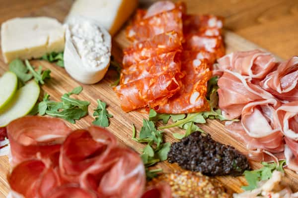 Artisan charcuterie board featuring sliced meats, cheeses, olives, spreads, and apple slices on a wooden cutting board.