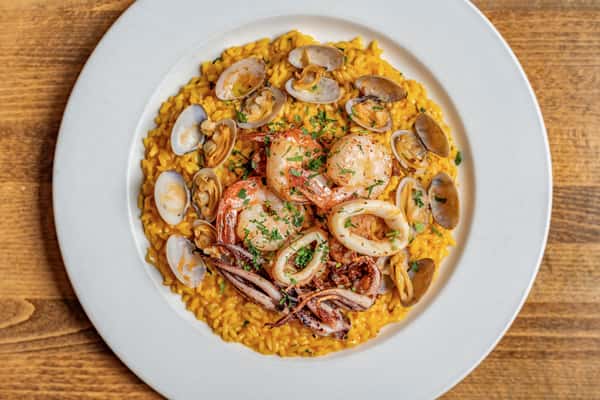 Top-down shot of golden saffron risotto topped with sautéed shrimp, squid, and clams, garnished with herbs—authentic Italian seafood risotto perfect for elegant menu listings.