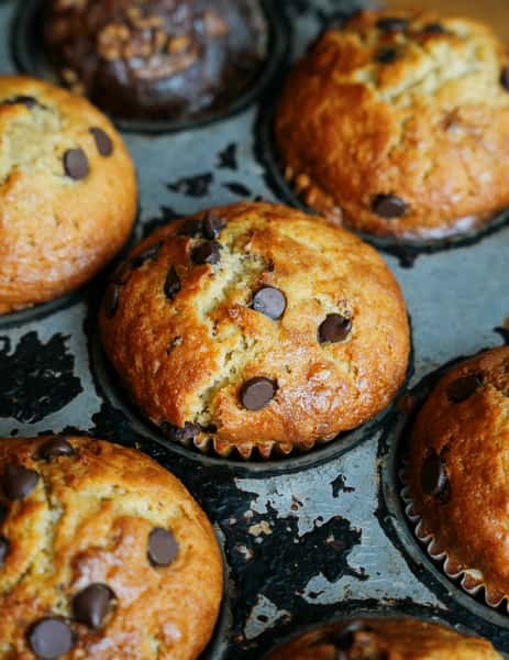 Close-up of freshly baked chocolate chip muffins in a rustic muffin tin, highlighting golden tops and rich chocolate chunks.
