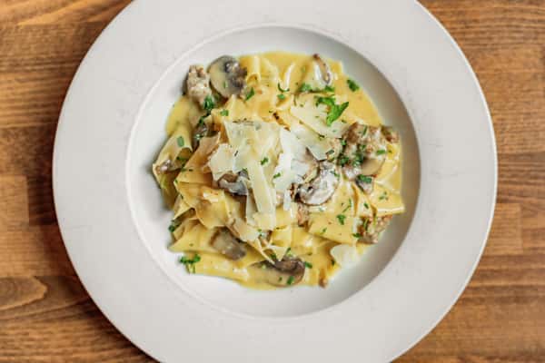 Overhead view of pappardelle pasta tossed in a creamy mushroom and sausage sauce, topped with shaved Parmesan and fresh parsley—rich and savory Italian pasta dish ideal for fall and winter menus.