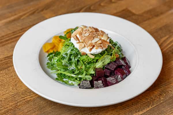 Goat cheese arugula salad with sliced almonds and vibrant red and yellow beets, served fresh on a white plate.