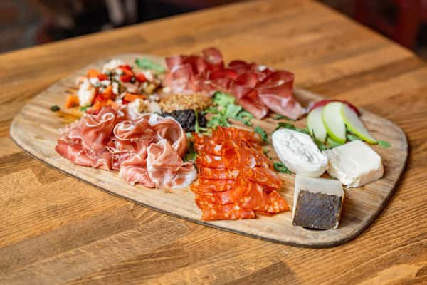 Rustic Italian charcuterie board featuring thinly sliced prosciutto, spicy salami, aged cheeses, creamy goat cheese, marinated vegetables, and fresh pear slices, artfully arranged on a wooden board — perfect for an antipasto appetizer or wine pairing.