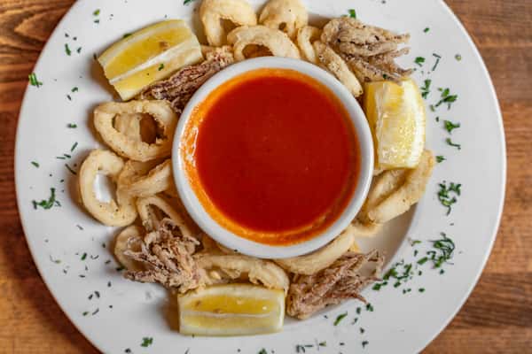 Crispy fried calamari rings served with lemon wedges and a side of zesty marinara sauce, garnished with fresh parsley on a white plate — perfect appetizer in Italian seafood cuisine.