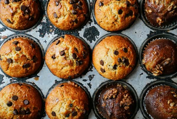 Close-up of a rustic muffin tray filled with golden chocolate chip and walnut muffins, fresh from the oven.