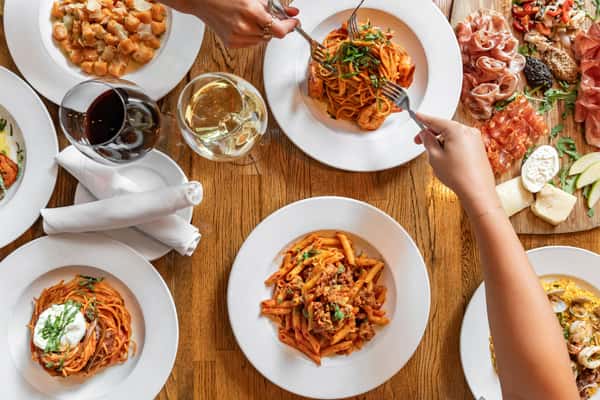 Top-down view of a rustic Italian feast including pasta dishes, charcuterie, salads, and wine glasses on a wooden table.