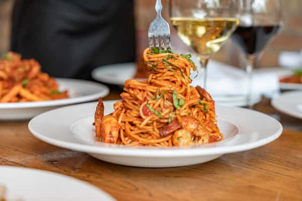 Twirl of spaghetti with shrimp in a rich tomato sauce, garnished with fresh basil, paired with glasses of white and red wine — elegant Italian seafood pasta dish served at a fine dining restaurant.