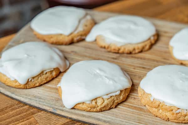 Close-up of soft, round sugar cookies generously topped with smooth white icing, arranged neatly on a wooden tray for a bakery display or seasonal treat.