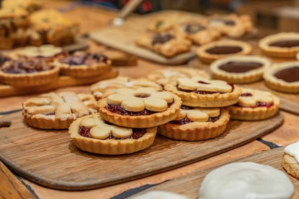 Assortment of buttery jam-filled cookies topped with daisy-shaped shortbread, arranged on a rustic wooden tray—ideal for a bakery display or seasonal dessert menu.