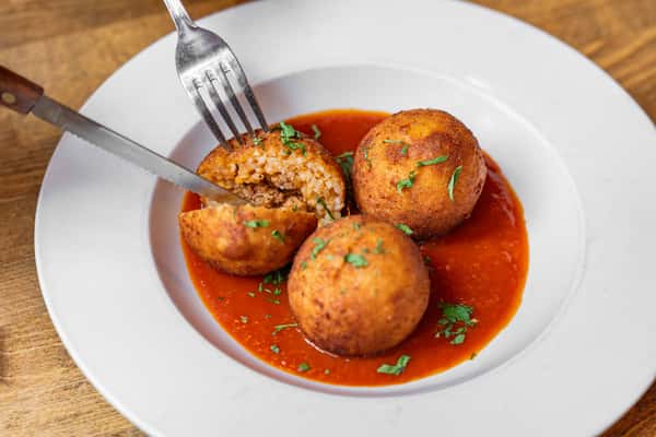 Classic Italian arancini—crispy rice balls with a savory filling, plated with rich tomato sauce and garnished with parsley.