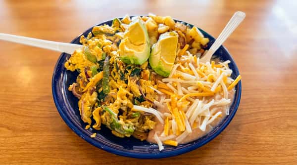 Breakfast plate with scrambled eggs, bell peppers, onions, avocado slices, home fries, refried beans, and shredded cheese.