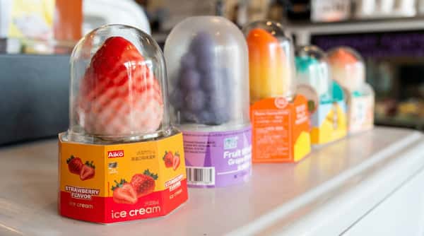 A row of fruit-shaped ice cream containers under clear domes, including strawberry and grape flavors.