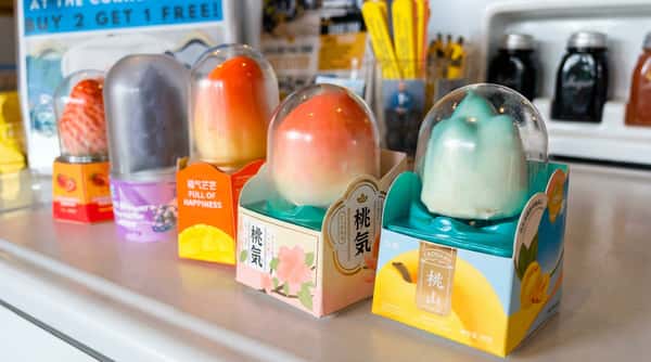 A row of individually packaged peach-shaped ice cream desserts in clear plastic domes and colorful boxes.