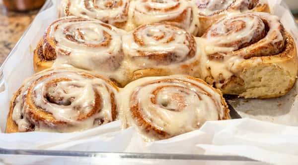 A pan of warm cinnamon rolls with white cream cheese frosting, some spilling over the edges.