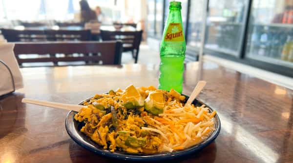 A breakfast plate with scrambled eggs, diced potatoes, avocado, refried beans with shredded cheese, and a green Squirt soda.