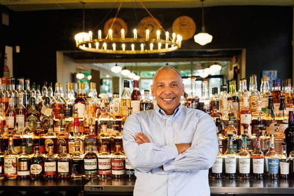 Owner standing in front of Serafini's fully stocked bar, showcasing the warm hospitality of the Italian fusion restaurant in downtown Frankfort, Kentucky.
